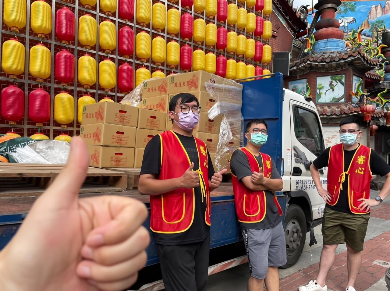 三位穿著紅色背心的志工在裝載紙箱的貨車旁合影