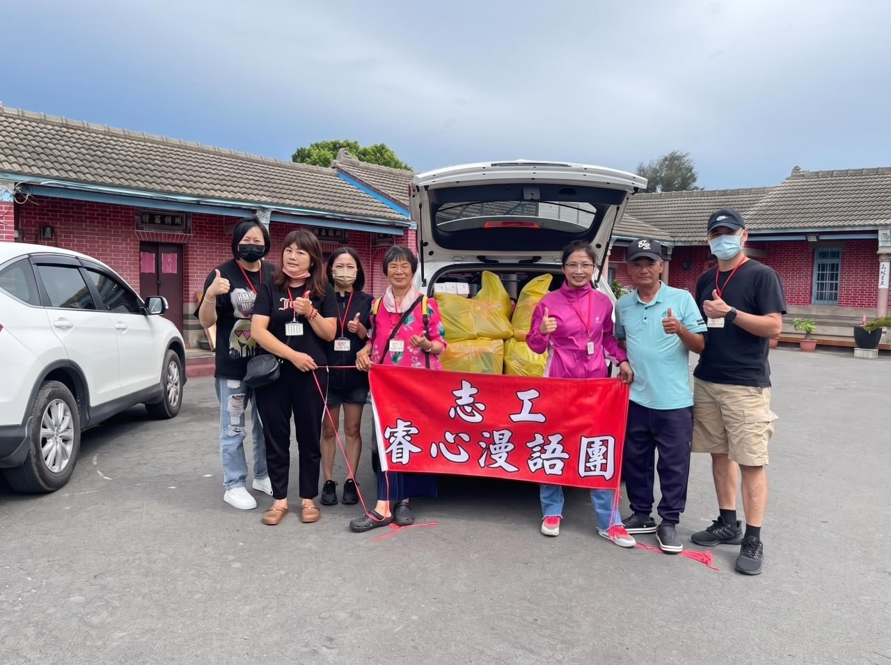志工在裝載物資的車輛前持團體旗幟合影